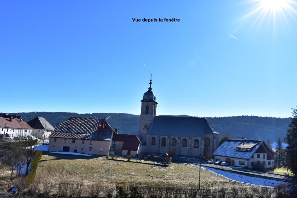 une église avec une tour au sommet d'une colline dans l'établissement bel appartement dans la montagne, L'orée du Bois, à Mouthe