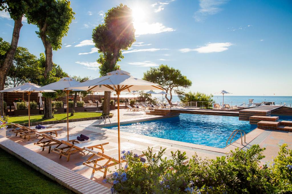- une piscine avec des tables et des parasols à côté de l'océan dans l'établissement Hotel Excelsior Venice, sur le Lido de Venise
