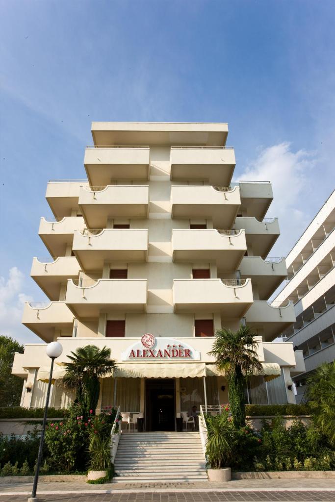 un grand bâtiment blanc avec des palmiers devant dans l'établissement Hotel Alexander, à Cattolica