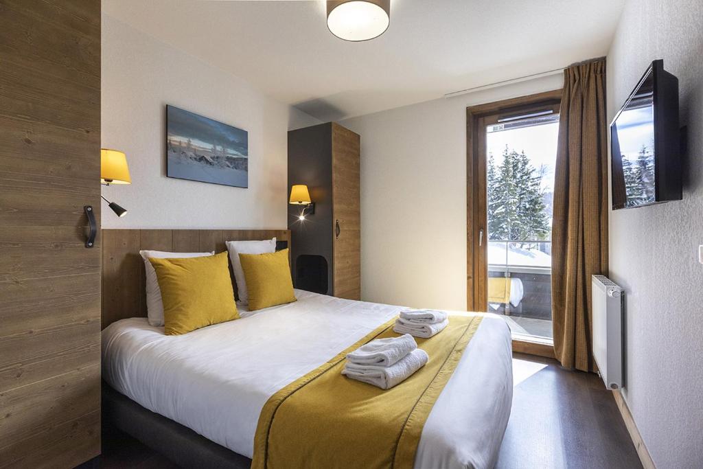 une chambre avec un lit avec des oreillers jaunes et une fenêtre dans l'établissement Résidence Club MMV Les Chalets des Cimes, aux Saisies