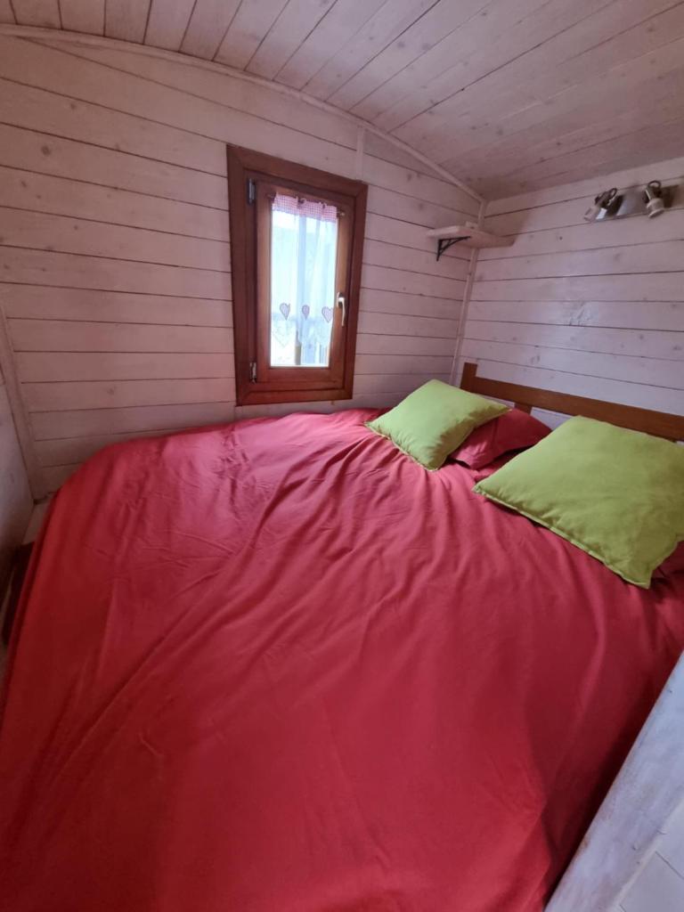 Cette chambre comprend un grand lit rouge et une fenêtre. dans l'établissement Roulotte du domaine de la Graou, à La Palud-sur-Verdon