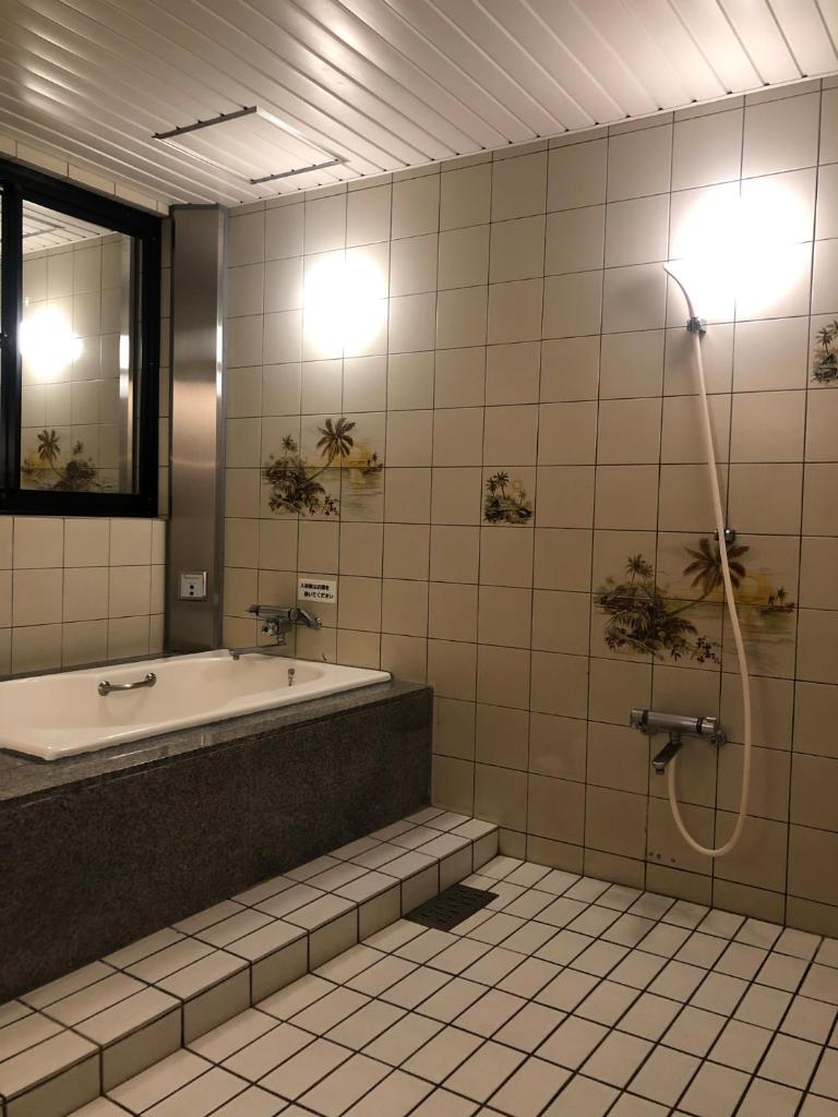 une salle de bain avec baignoire et douche dans l'établissement ホテルハンズ, à Ginan