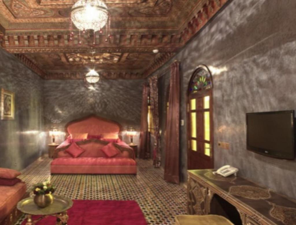 Cette chambre comprend un lit rouge et une télévision. dans l'établissement Mumtaz Mahal, à Essaouira