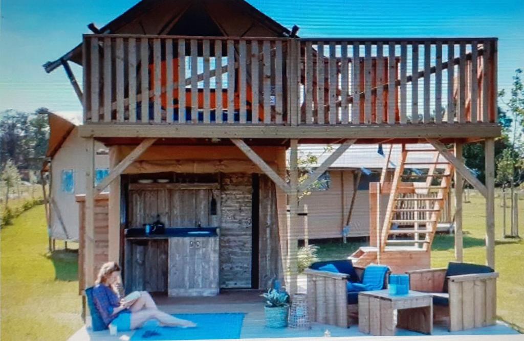 une femme assise sur une chaise devant une cabane dans les arbres dans l'établissement Tente Cabane du Camping Hautoreille, à Bannes