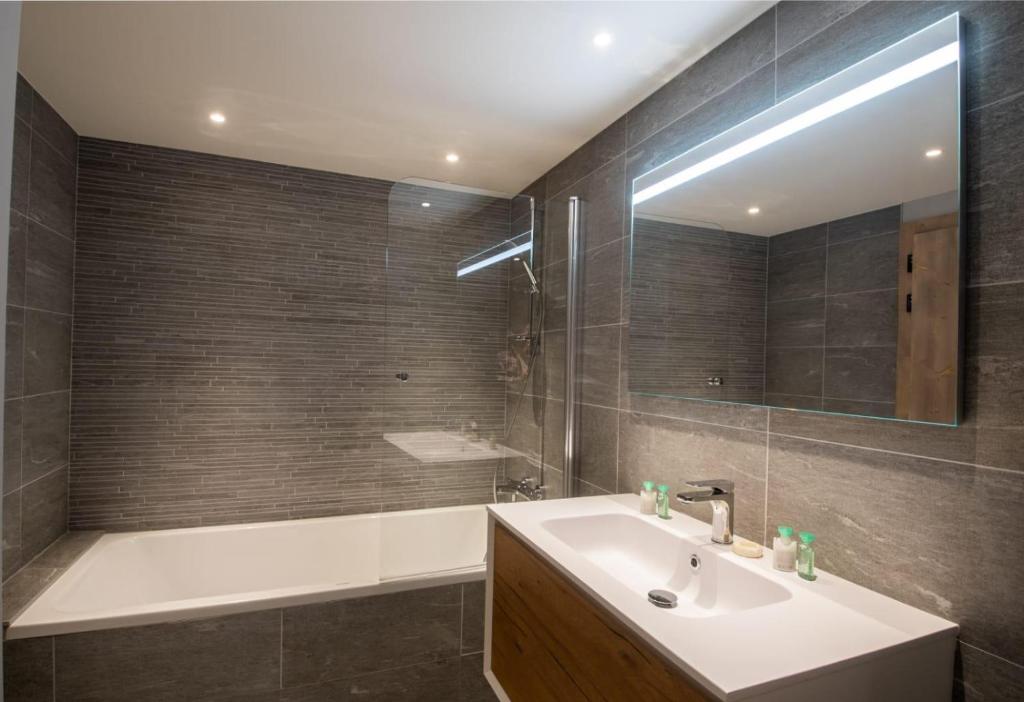 une salle de bain avec un lavabo, une baignoire et un miroir dans l'établissement Luxueux appartement skis aux pieds, jacuzzi privatif, à Courchevel