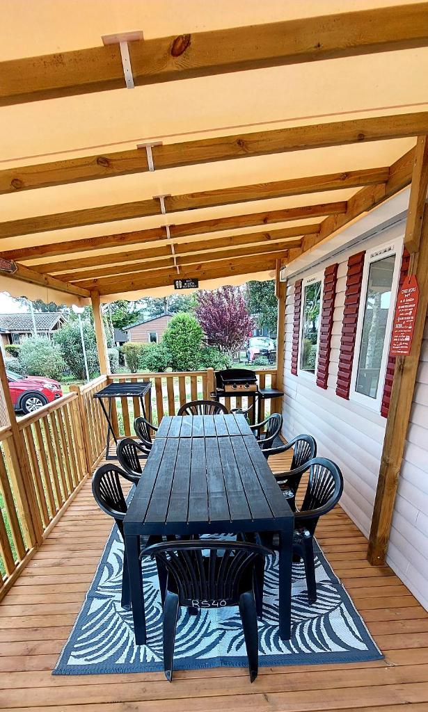 une table et des chaises noires sur une terrasse en bois dans l'établissement Mobil Home Camping Les VIVIERS, Claouey, à Claouey