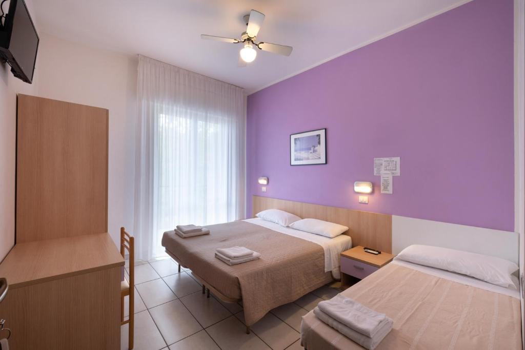 une chambre d'hôtel avec deux lits et des murs violets dans l'établissement Hotel Giordo, à Rimini