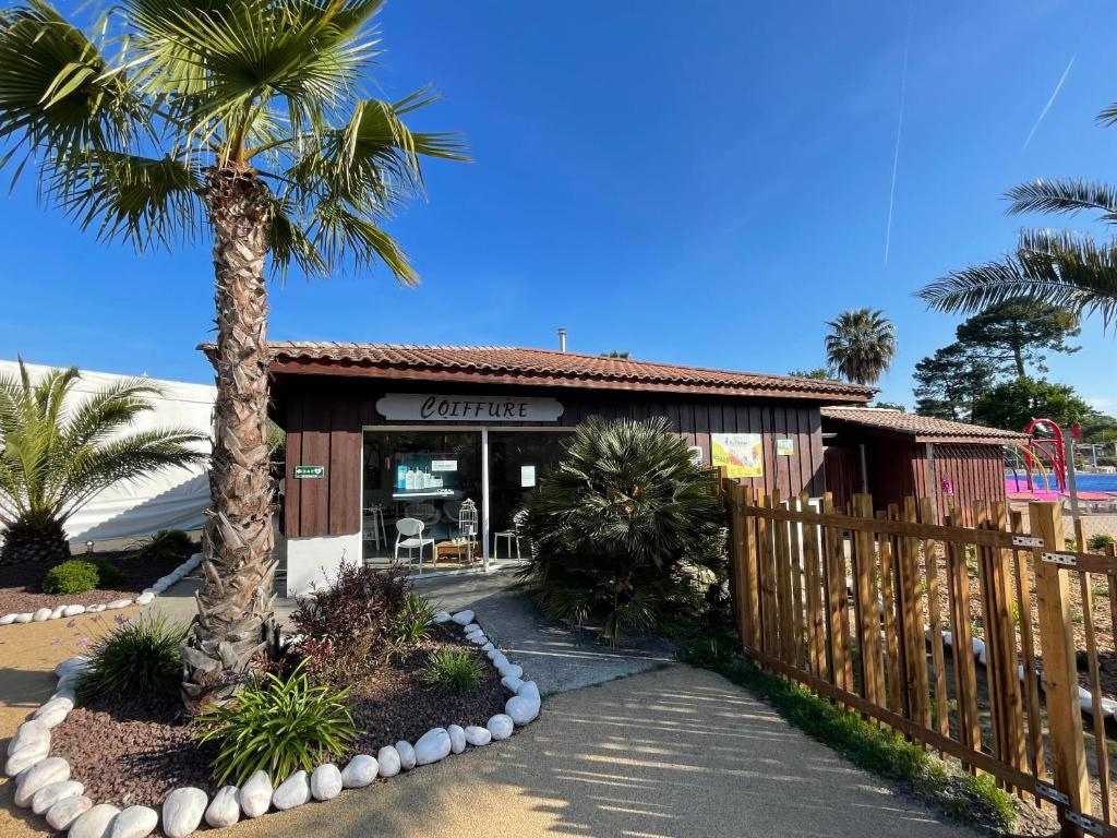 un bâtiment avec une clôture et un palmier dans l'établissement Mobil home XXL - Bord LAC - CAMPING Les Viviers - Lège cap ferret, à Lège-Cap-Ferret