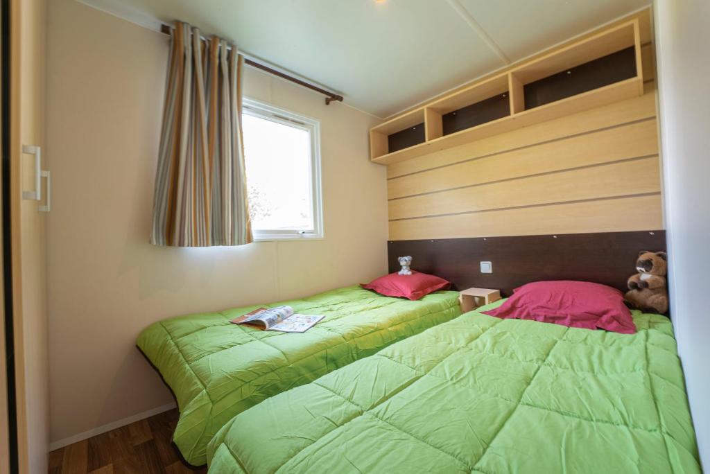 - 2 lits dans une chambre avec des draps verts et des oreillers roses dans l'établissement Camping New Rabioux, à Châteauroux-les-Alpes