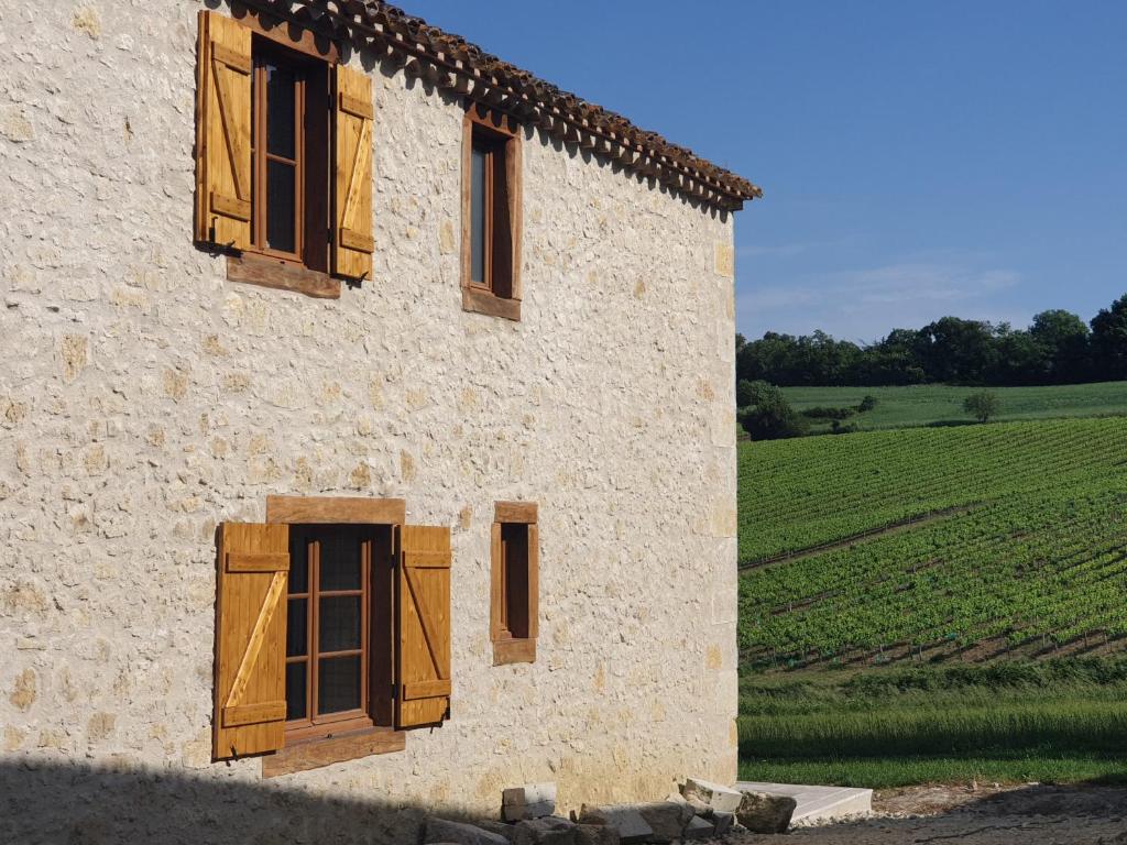 un bâtiment avec des fenêtres en bois et un champ de cultures dans l'établissement Gite La Halippe, à Caussens