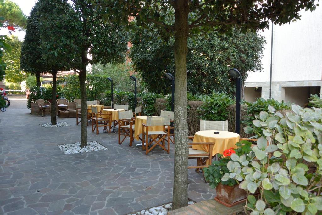 un groupe de tables et de chaises plantées d'arbres et de fleurs dans l'établissement Hotel Alisei, à Lignano Sabbiadoro