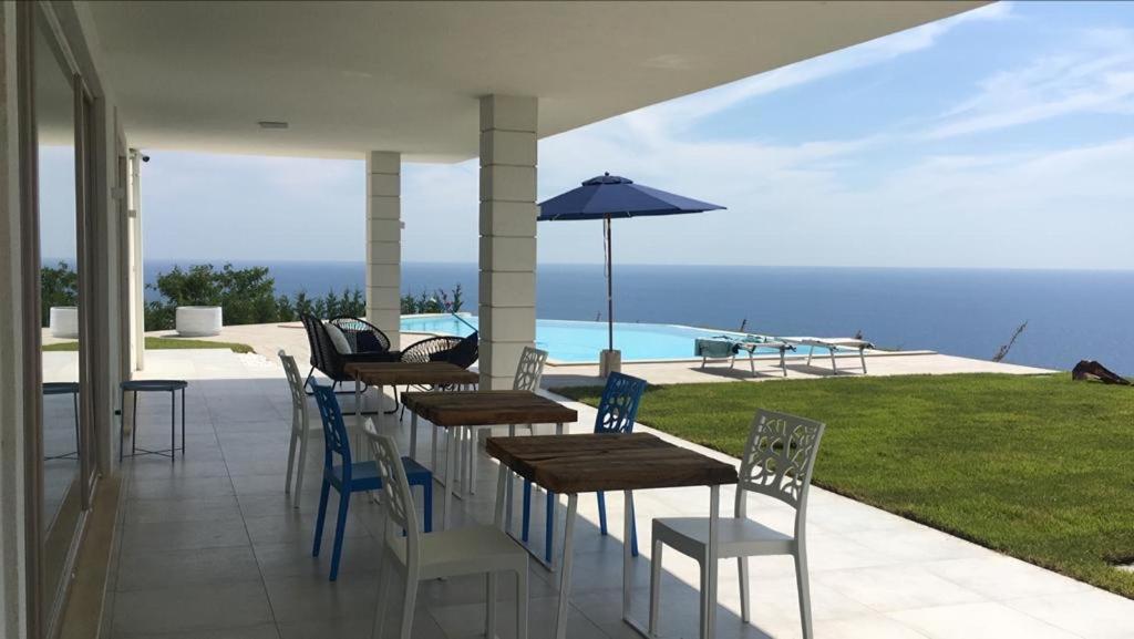 un patio avec tables, chaises et un parasol dans l'établissement Luxury villa Blue&Blanc piscina a sfioro isola, à Diamante