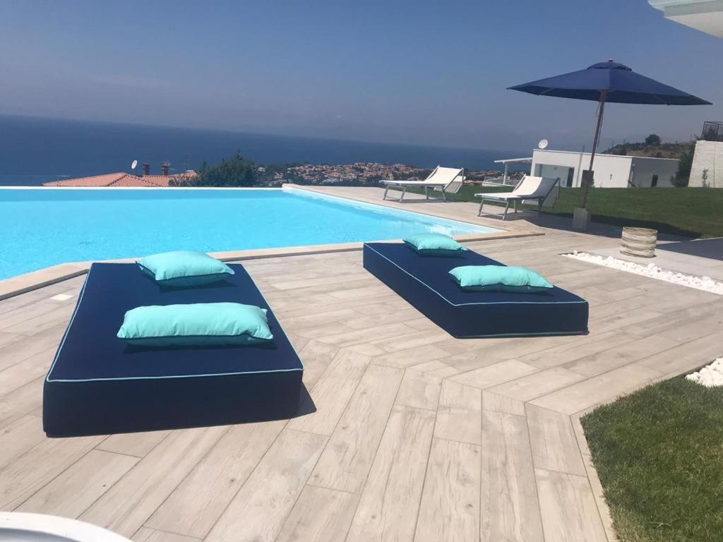 - deux oreillers installés sur une terrasse en bois à côté de la piscine dans l'établissement Luxury villa Blue&Blanc piscina a sfioro isola, à Diamante