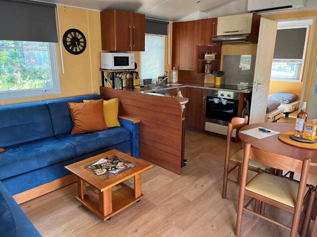 un salon avec un canapé bleu et une cuisine dans l'établissement Joli Mobil-Home de Vacances, Ideal pour les familles, à Rocbaron