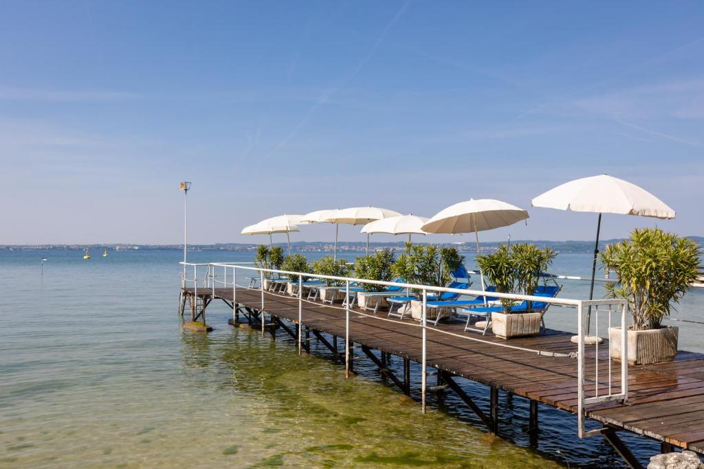 une jetée avec des chaises et des parasols sur l'eau dans l'établissement Hotel Serenella, à Sirmione