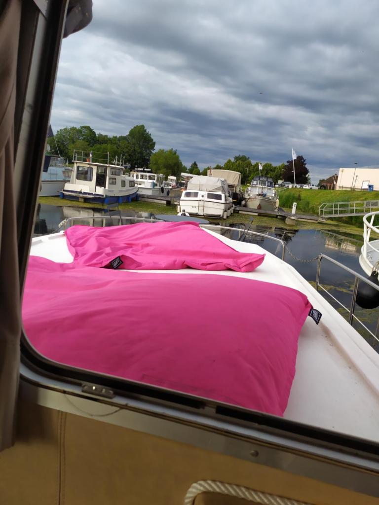 - un lit sur un bateau avec une couverture rose dans l'établissement Penichette habitable max 4-5 pers terrasse vue sur l'eau ST JEAN DE LOSNE, à Saint-Jean-de-Losne