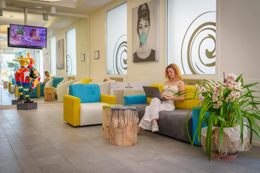 une femme assise sur un canapé dans le hall avec un ordinateur portable dans l'établissement Design Hotel Astra B&B, à Misano Adriatico
