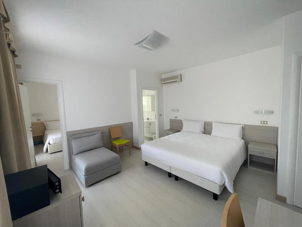 une chambre blanche avec un lit et une chaise dans l'établissement Hotel Athena, à Lignano Sabbiadoro