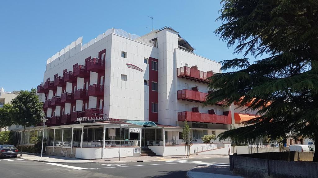 un grand bâtiment blanc avec une voiture garée devant. dans l'établissement Hotel Vienna, à Lignano Sabbiadoro