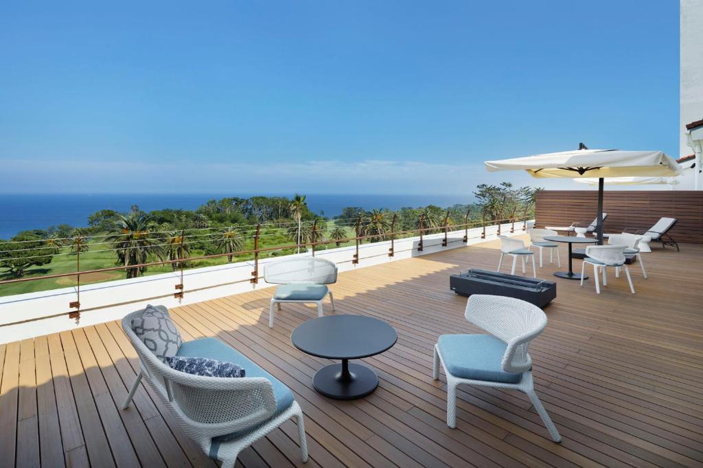 une terrasse avec des chaises, des tables et un parasol dans l'établissement Kawana Hotel, à Itō