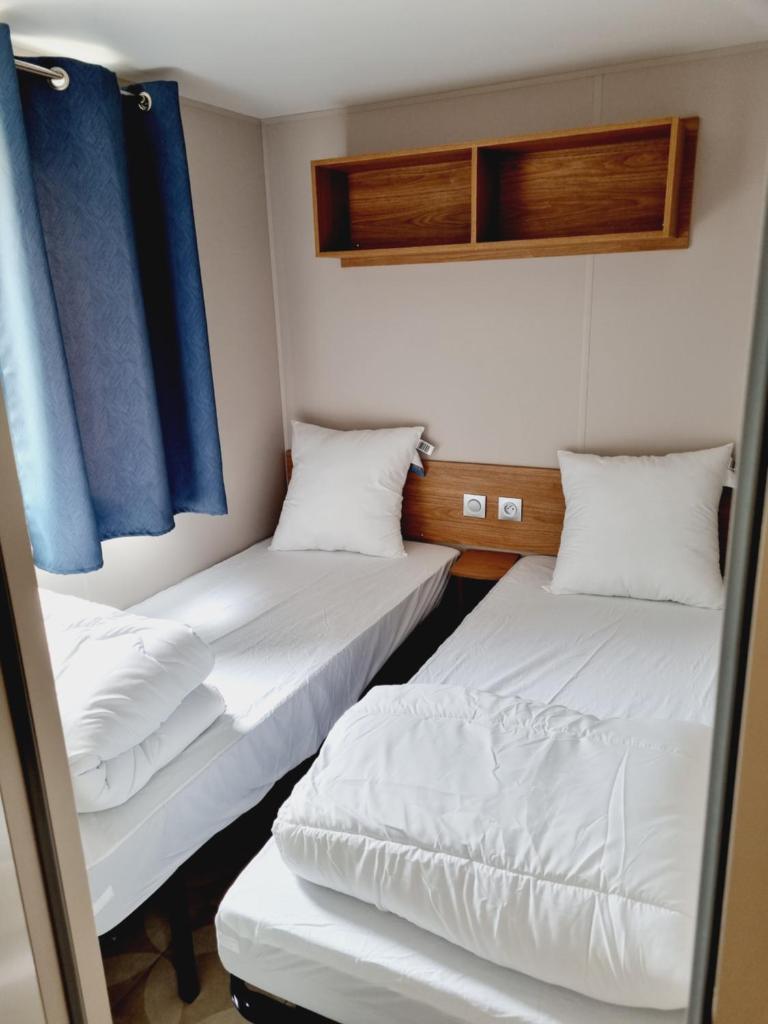 - 2 lits dans une petite chambre avec des rideaux bleus dans l'établissement Mobil home camping Les ViVIERS Cap Ferret, à Claouey 26 autres photos