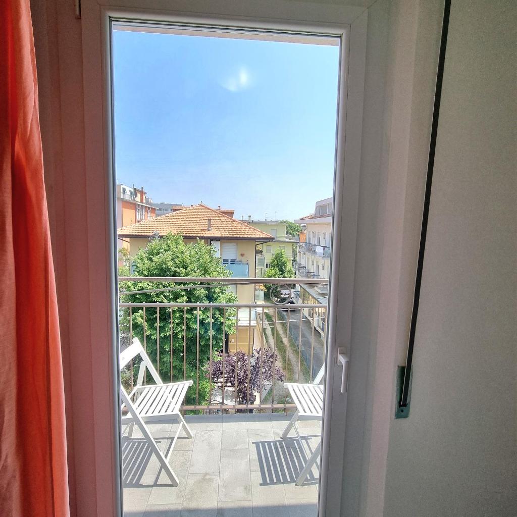 une porte coulissante en verre s'ouvrant sur un balcon avec deux chaises. dans l'établissement Residence Mare, à Rimini