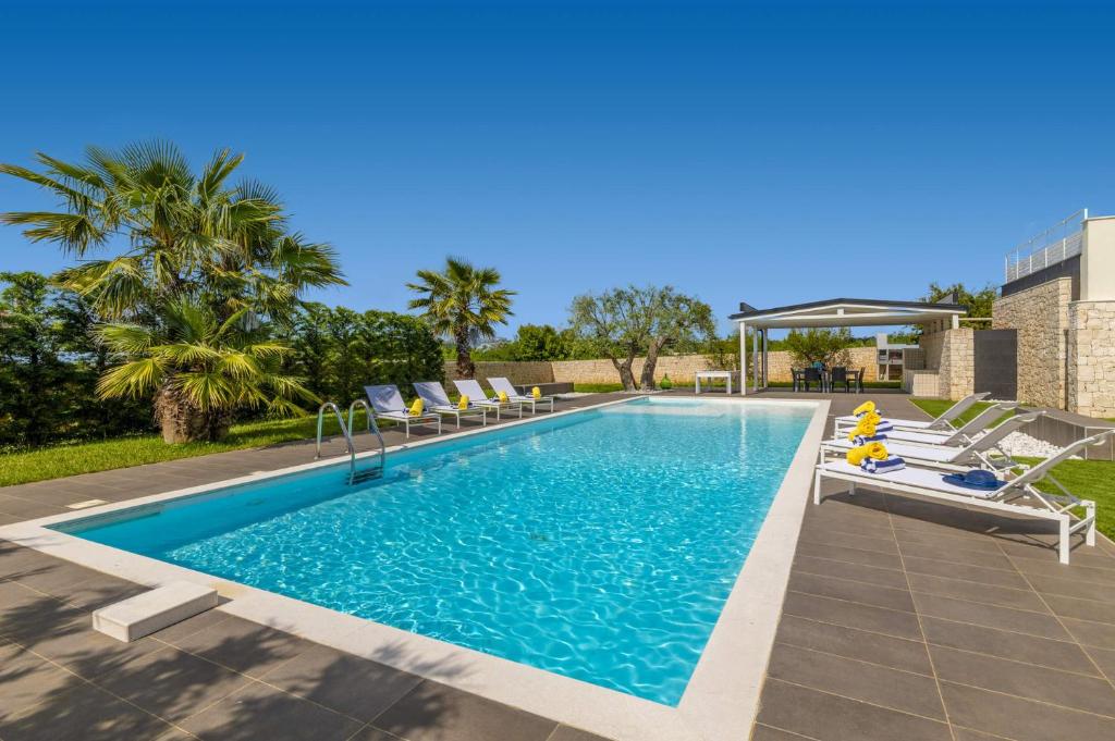 une piscine avec chaises longues et palmiers dans l'établissement Villa Campanella by Villa Plus, à Noci