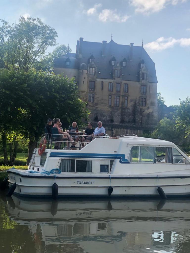 un groupe de personnes sur un bateau dans l'eau avec un château dans l'établissement Le bateau du Foudre, à Châtillon-en-Bazois