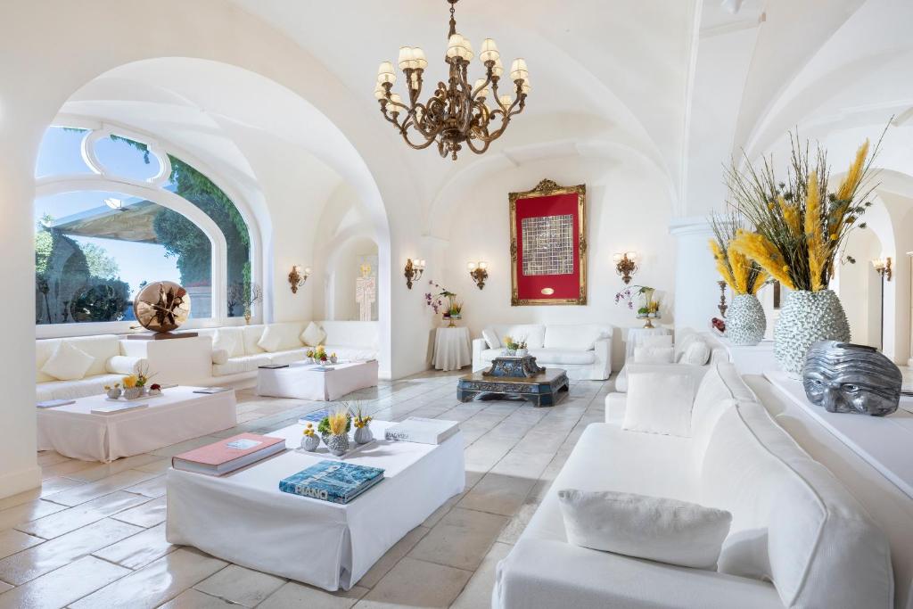 Elle comprend un salon doté d'un mobilier blanc et d'un lustre. dans l'établissement Jumeirah Capri Palace, à Anacapri