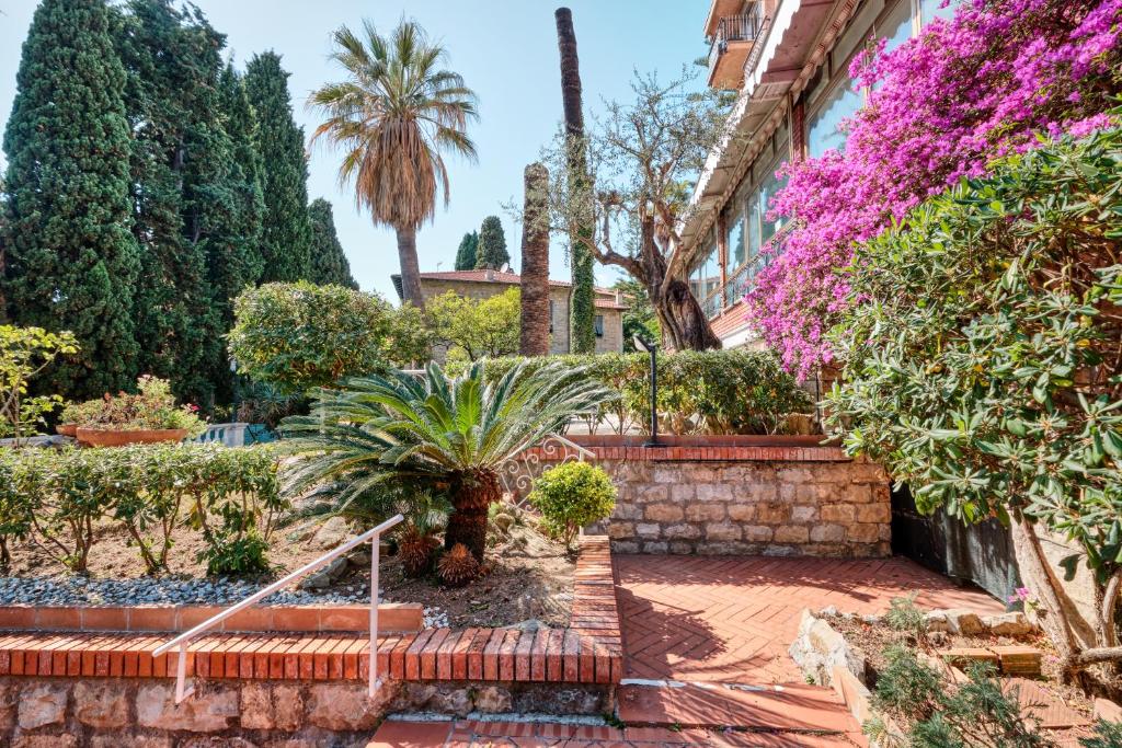 un jardin en face d'un bâtiment planté d'arbres et de fleurs dans l'établissement Hotel Astoria, à Bordighera