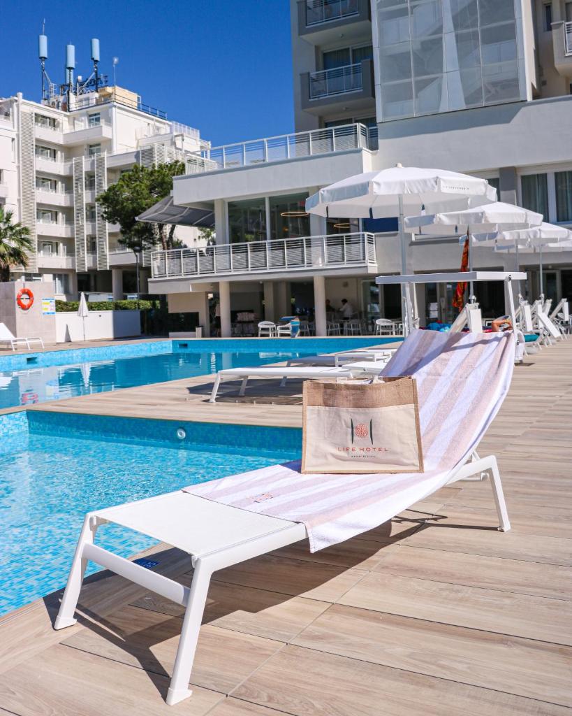 une chaise longue blanche assise à côté d'une piscine dans l'établissement Life Hotel 4 Superior, à Bibione