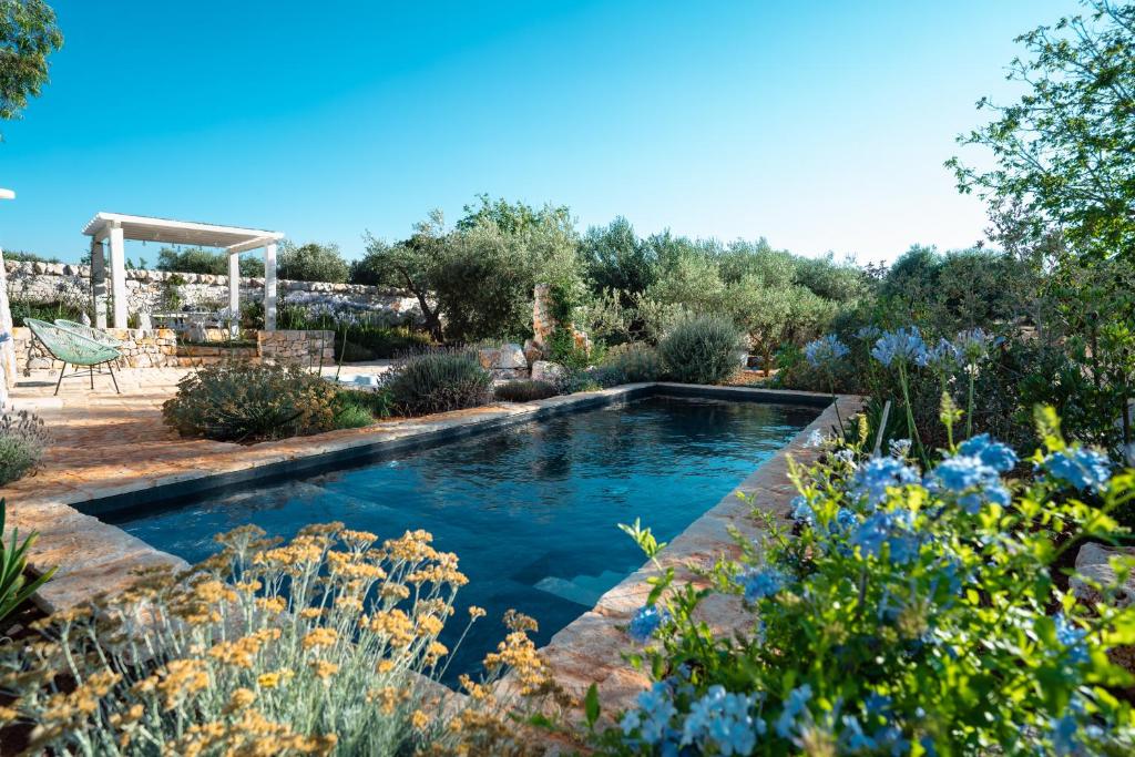 une piscine dans un jardin avec des fleurs bleues dans l'établissement Trulli Ad Maiora, à Alberobello