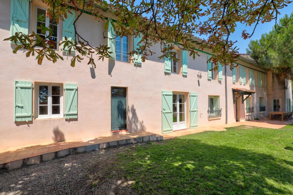 un bâtiment avec des fenêtres vertes à volets et une cour dans l'établissement Gîte la grappe Occitane - 14 personnes - piscine privée, à Ambres