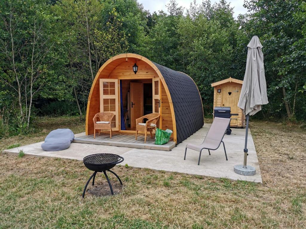 une petite tente avec une chaise et un parasol dans l'établissement Charmant POD en bois près d'un plan d'eau, à Nielles-lès-Ardres