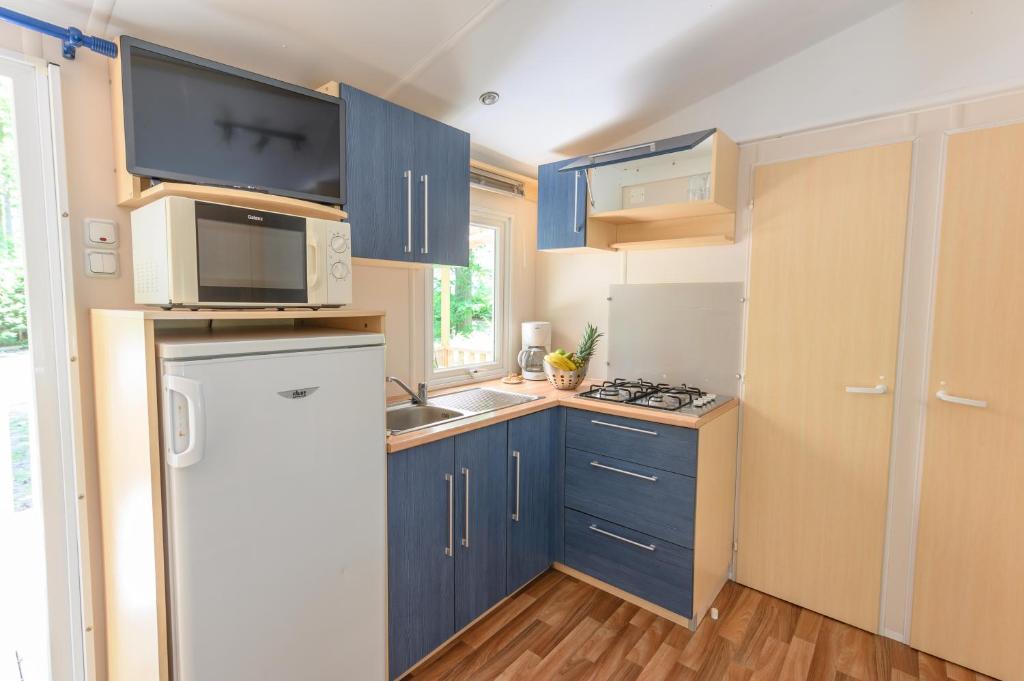 Elle comprend une petite cuisine avec des placards bleus et un réfrigérateur blanc. dans l'établissement Mobil-home le ROBINSON, à Mirgaudon