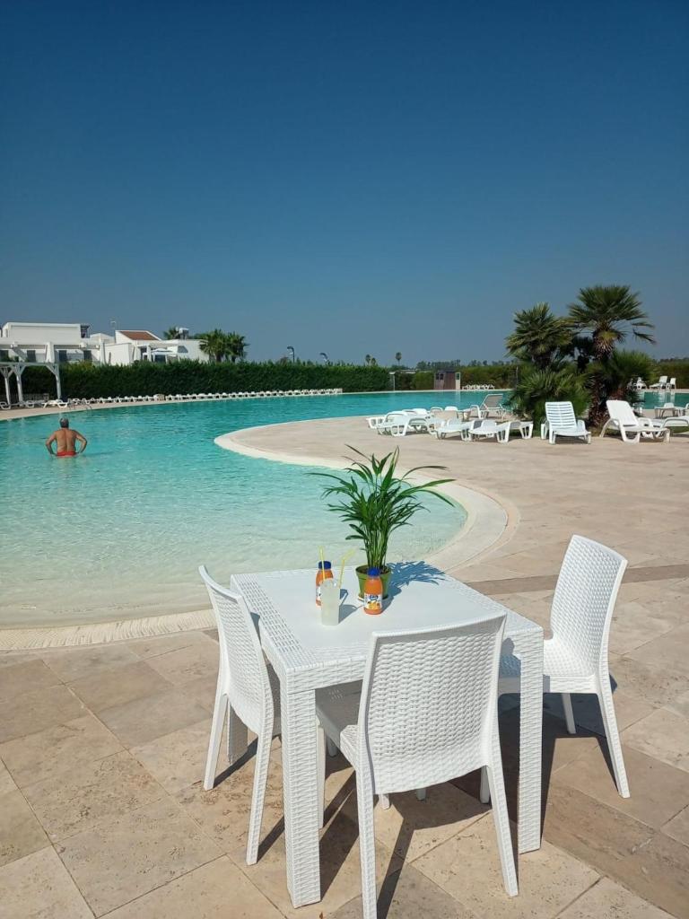 - une table et des chaises blanches à côté de la piscine dans l'établissement I GIARDINI DI ZEUS, à Métaponte