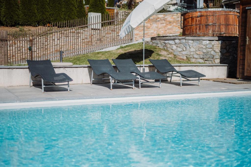 quatre chaises et un parasol à côté d'une piscine dans l'établissement Résidence Sunêlia Les Logis d'Orres, aux Orres