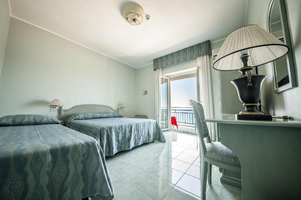 une chambre avec deux lits et un bureau et une fenêtre dans l'établissement Hotel Murano, à Rossano