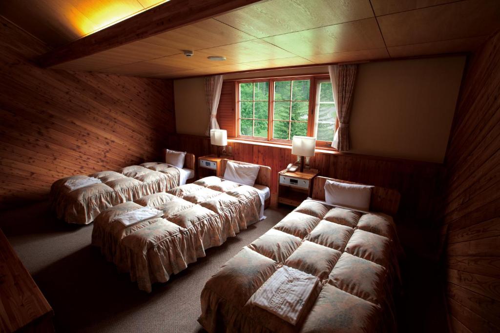 Cette chambre comprend 4 lits et une fenêtre. dans l'établissement Log Hotel Larch Lake Kanayama, à Minamifurano
