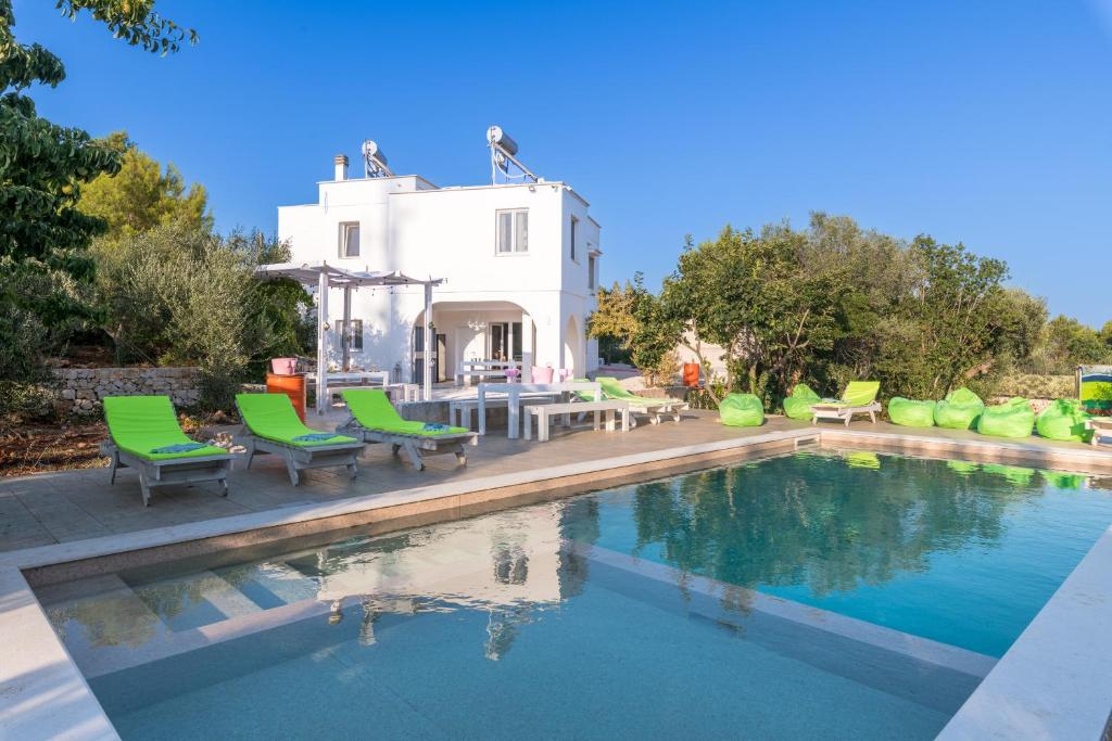 une piscine avec des chaises vertes et une maison dans l'établissement Ostuni Hills Boutique Villa-AC in every room, à Ostuni