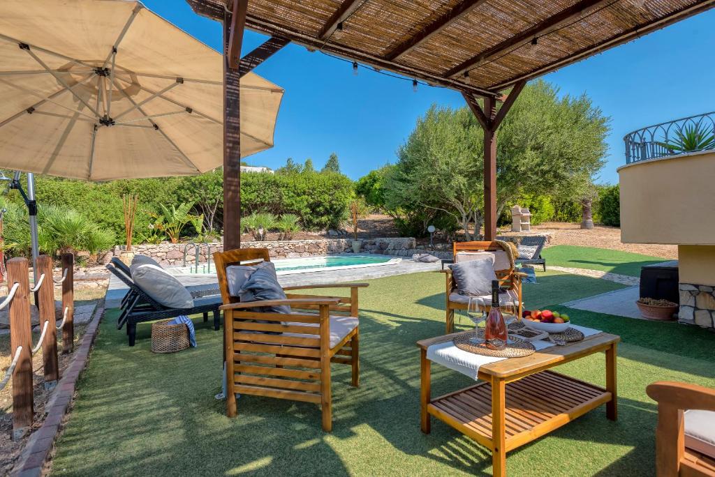 un patio avec des chaises, une table et un parasol dans l'établissement Villa Pedra Alghero - appartamento in villa con piscina, à Alghero