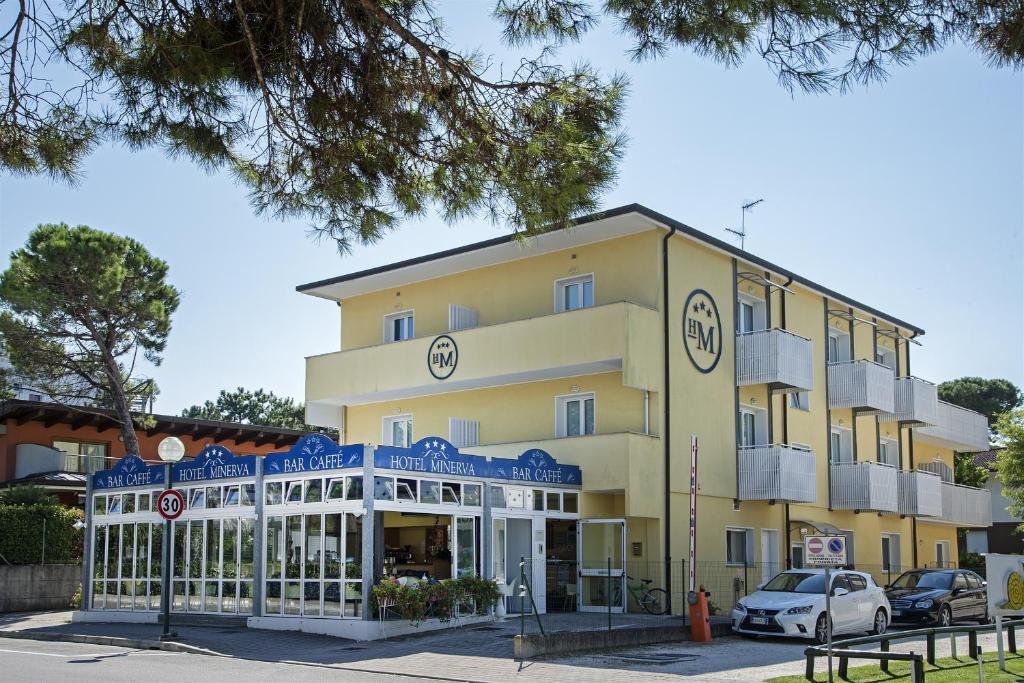 un grand bâtiment jaune avec une façade de magasin dans l'établissement Hotel Minerva, à Lignano Sabbiadoro
