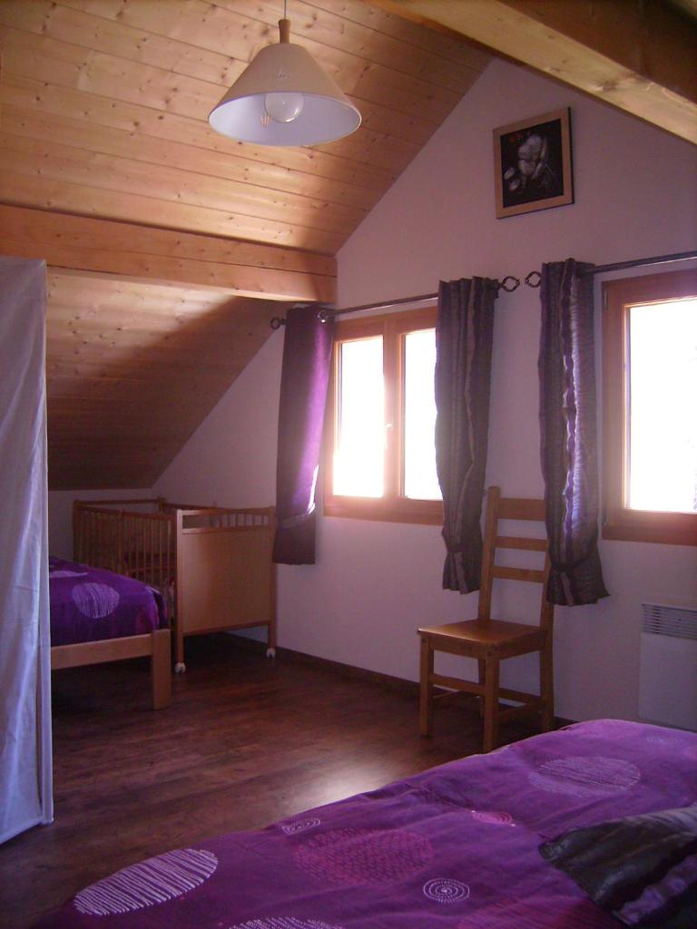 une chambre avec un lit, une chaise et des fenêtres dans l'établissement Gite du Brin d'Herbe, à Pontarlier