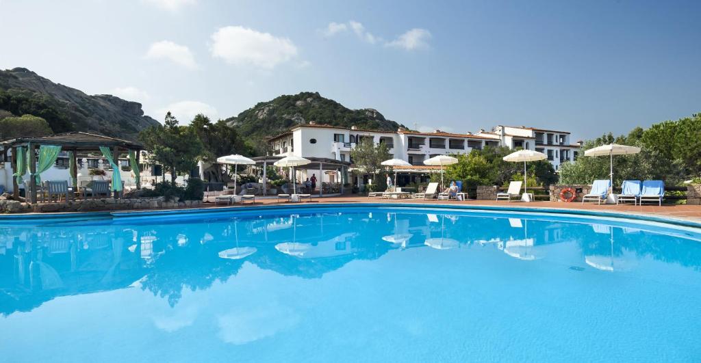 une grande piscine bleue avec chaises et parasols dans l'établissement Hotel La Bisaccia, à Baja Sardinia