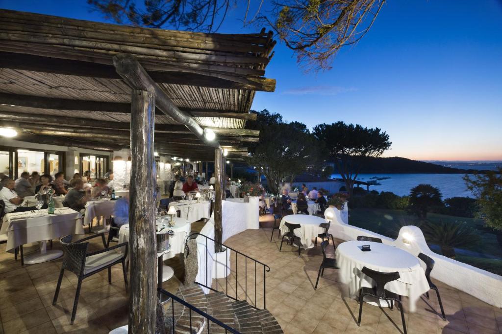 un restaurant avec des tables et des chaises blanches sur la terrasse dans l'établissement Hotel La Bisaccia, à Baja Sardinia