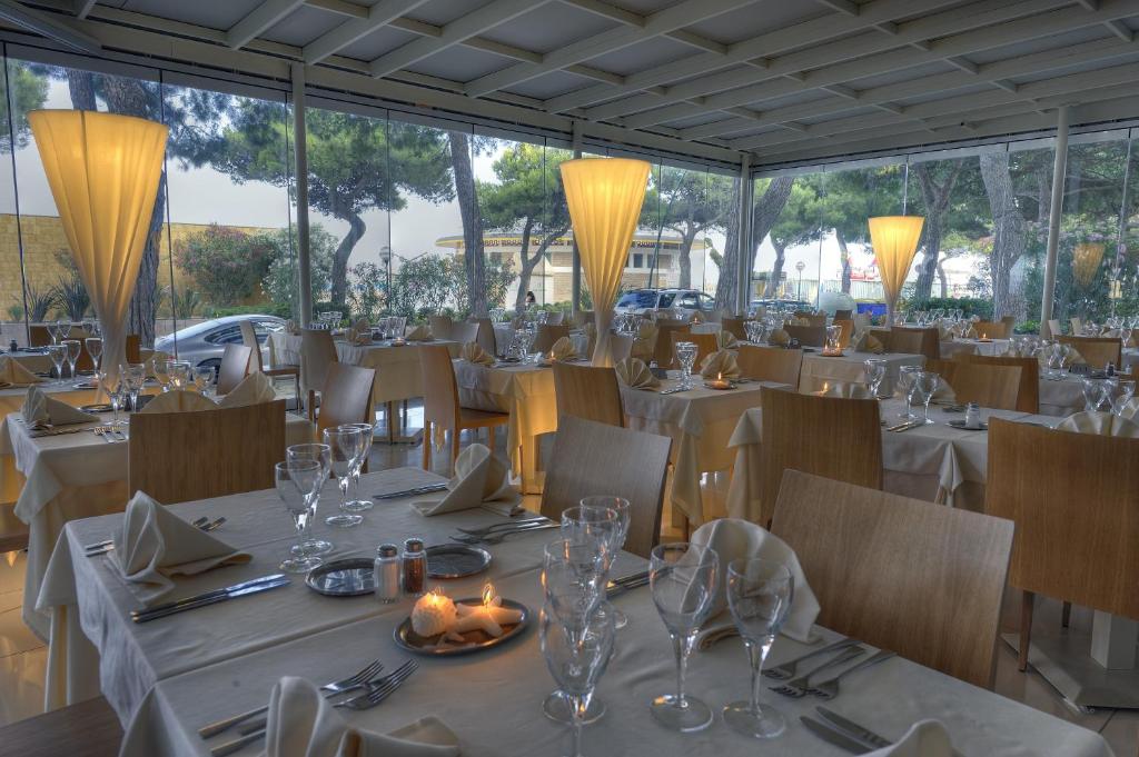 un restaurant avec des tables et des chaises blanches et des fenêtres dans l'établissement Hotel Europa Lignano, à Lignano Sabbiadoro