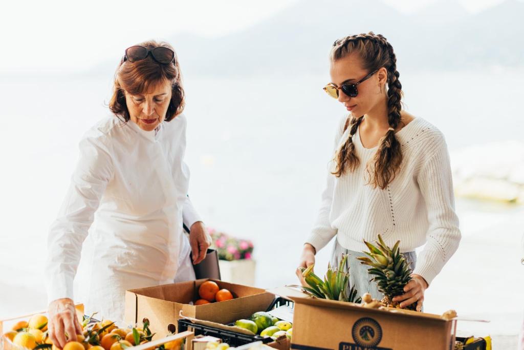 deux femmes debout à côté de caisses de fruits et légumes dans l'établissement Hotel Orione - Lake Front Hotel, à Brenzone 84 autres photos