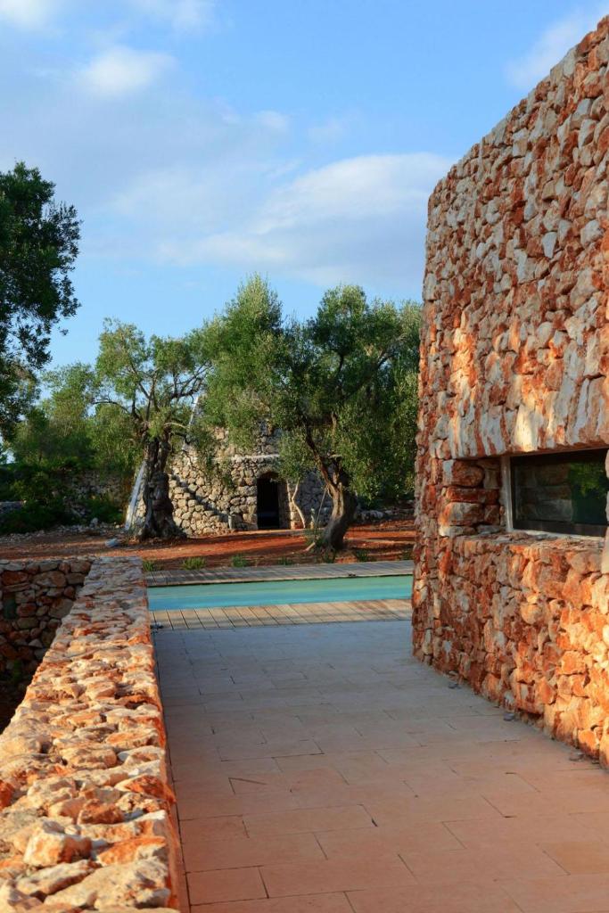 un bâtiment en pierre avec un mur en pierre et des arbres en arrière-plan dans l'établissement Bosco degli Ulivi, à Morciano di Leuca
