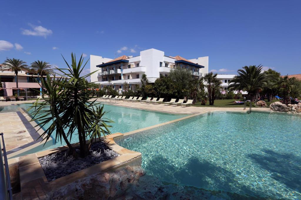 une piscine avec un palmier devant un immeuble dans l'établissement Villaggio Giardini D'Oriente, à Nova Siri Marina