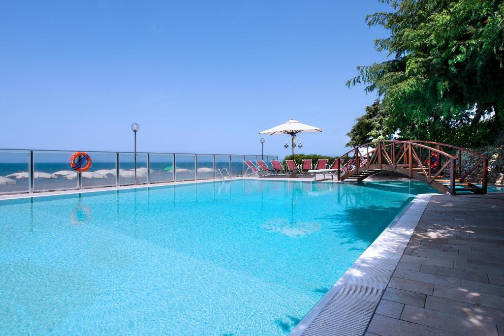 une grande piscine bleue à côté de l'océan dans l'établissement Hotel I Ginepri, à Marina di Castagneto Carducci